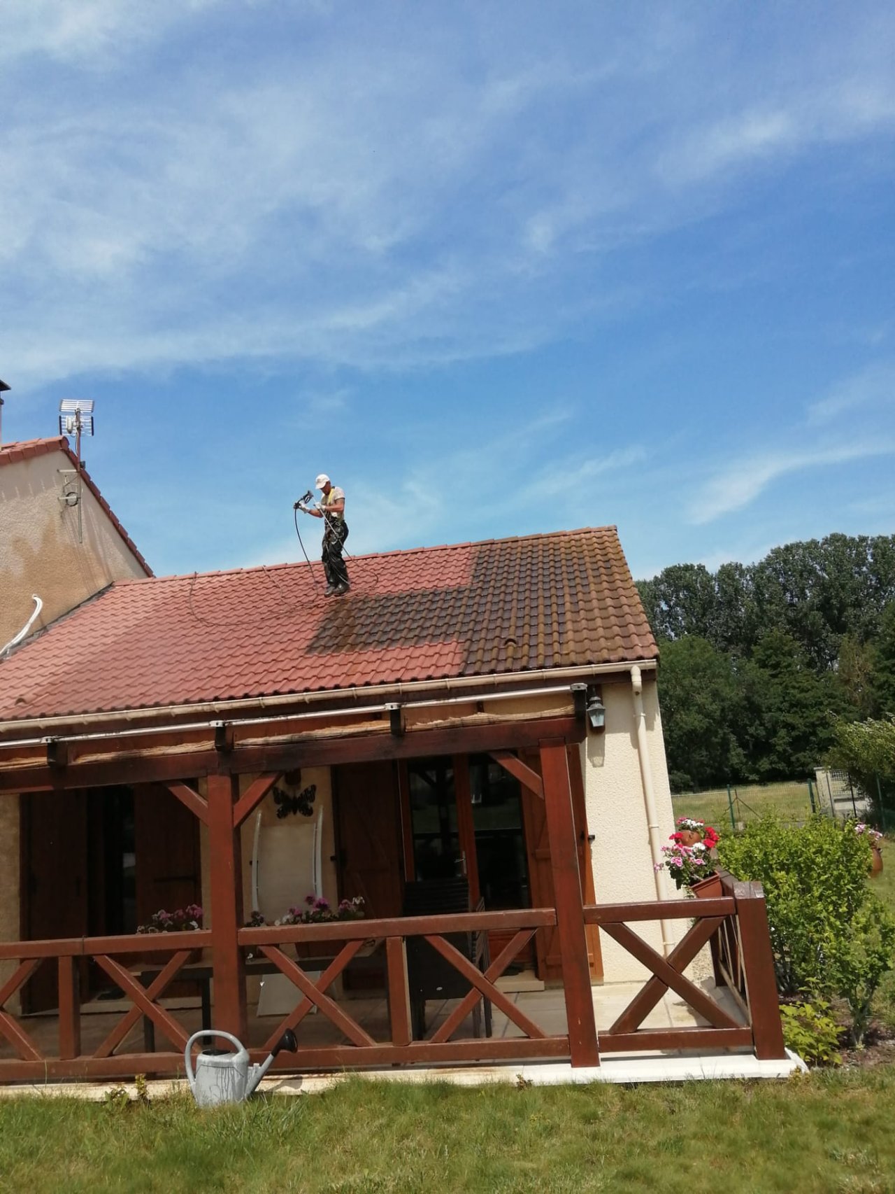 Couvreur au travail sur la toiture en tuiles d'une maison meusienne, jardin et arbres en arrière-plan