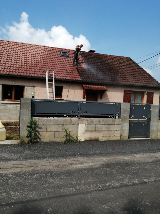 Artisan couvreur sur une toiture en tuiles d'une maison de village, vue depuis la rue